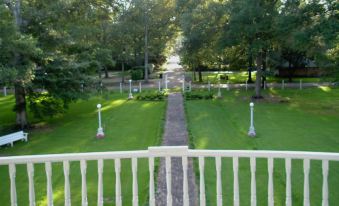 a white balcony overlooking a lush green garden with trees and a path leading up to it at Blythewood Plantation