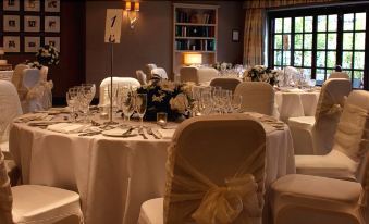 a well - decorated banquet hall with multiple tables covered in white tablecloths and adorned with various decorations , such as flowers and wine glasses at Manor Hotel