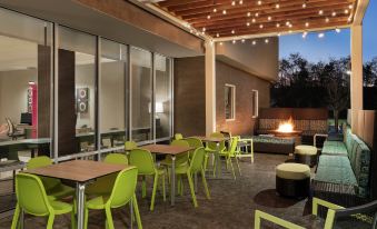 an outdoor patio area with green chairs and tables , a fire pit , and a large window at Home2 Suites by Hilton Harrisburg North