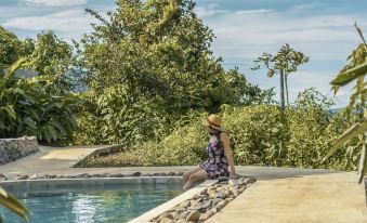 a woman in a hat is sitting on the edge of a pool with trees and trees in the background at La Tigra Rainforest Lodge