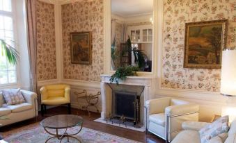 a living room with a fireplace , two chairs , and a painting on the wall , all decorated in white and gold at La Maison Rouge Broceliande