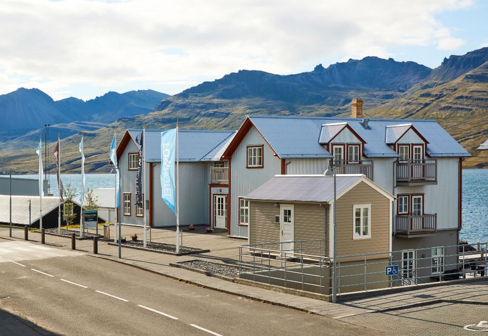 a row of houses with a blue roof are situated on a street with mountains in the background at Fosshotel Eastfjords