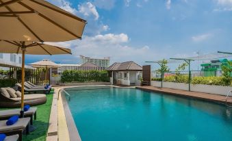 an outdoor swimming pool surrounded by a hotel , with lounge chairs and umbrellas placed around the pool area at Rattanachol Hotel