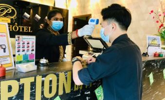 a man is checking in at a hotel , wearing a face mask and gloves , while a receptionist is checking in at Sem9 Senai "Formerly Known As Perth Hotel"