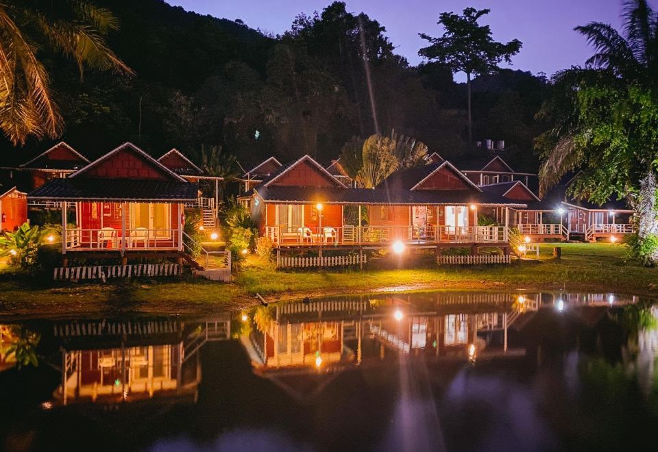 a row of small wooden houses surrounded by trees and water , illuminated by lights at night at Holiday Resort