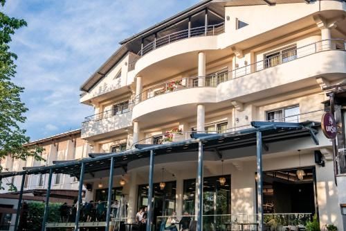 a group of people are standing outside a white building with balconies , enjoying the sunny day at Hotel THR Center