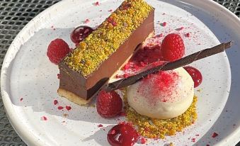 a white plate with a slice of chocolate cake , topped with raspberries and ice cream , placed on a dining table at Sibton White Horse Inn