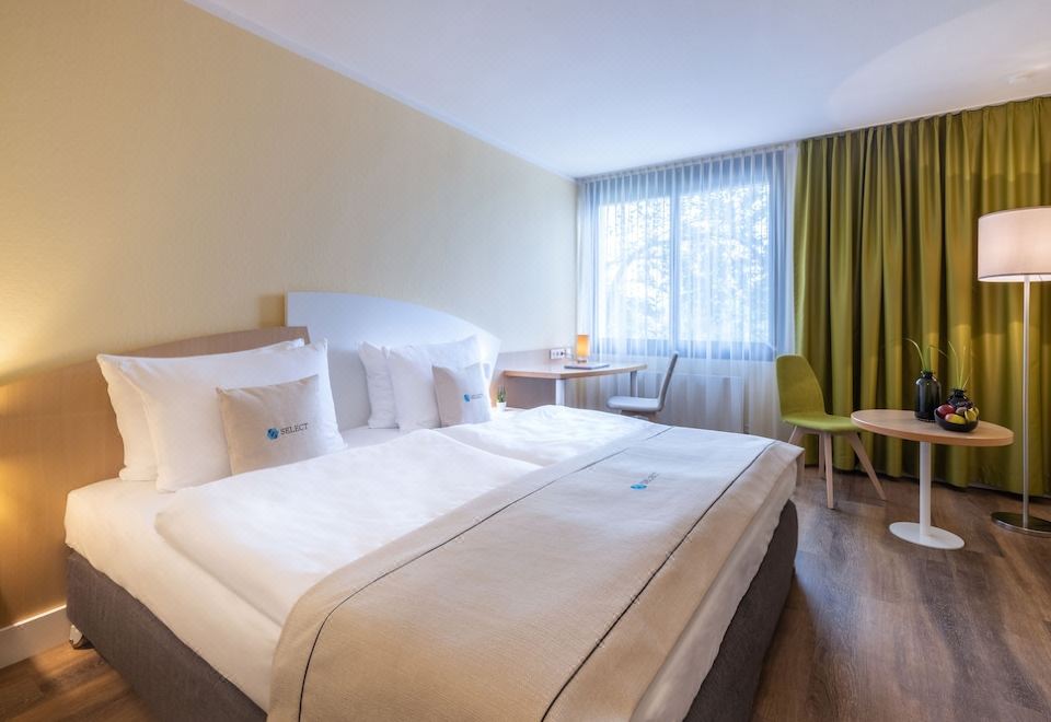 a large bed with white linens is in a room with a chair and window at Select Hotel Erlangen