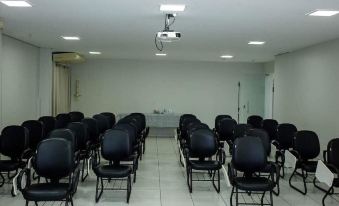 a large conference room with multiple rows of black chairs arranged in a semicircle , and a projector mounted on the ceiling at Maison Hotel