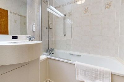 a bathroom with a white bathtub , shower , and sink , along with a towel on the counter at Village Hotel Liverpool