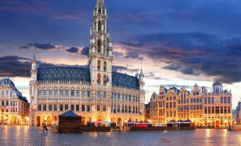 a large , ornate building with a tall tower is illuminated at night in a city square at Ibis Brussels Airport