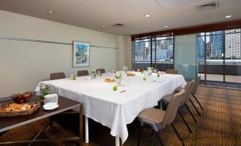 a conference room with a long table covered in a white tablecloth , surrounded by chairs and set for a meal at Ibis Sydney Darling Harbour
