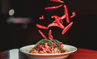 a plate of noodles with vegetables and red chili peppers is being lifted by a large umbrella at Holiday Inn Beach Resort