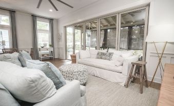 a spacious living room with white couches , a wooden coffee table , and large windows overlooking the outdoors at Magnolia Cottages by the Sea by Panhandle Getaways