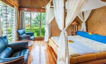 a bedroom with a canopy bed , wooden floors , and large windows overlooking a green landscape at Maravu Taveuni Lodge