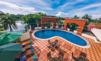 a large swimming pool with a red brick roof and surrounding outdoor furniture , including chairs and umbrellas at Hotel Grand Park Barishal