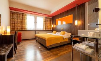 a modern hotel room with wooden floors , large windows , and an orange bedspread , accompanied by a desk and other amenities at Hotel Continental