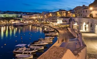 a picturesque harbor town at dusk , with numerous boats docked along the waterfront and restaurants lining the waterfront at Hotel Victori