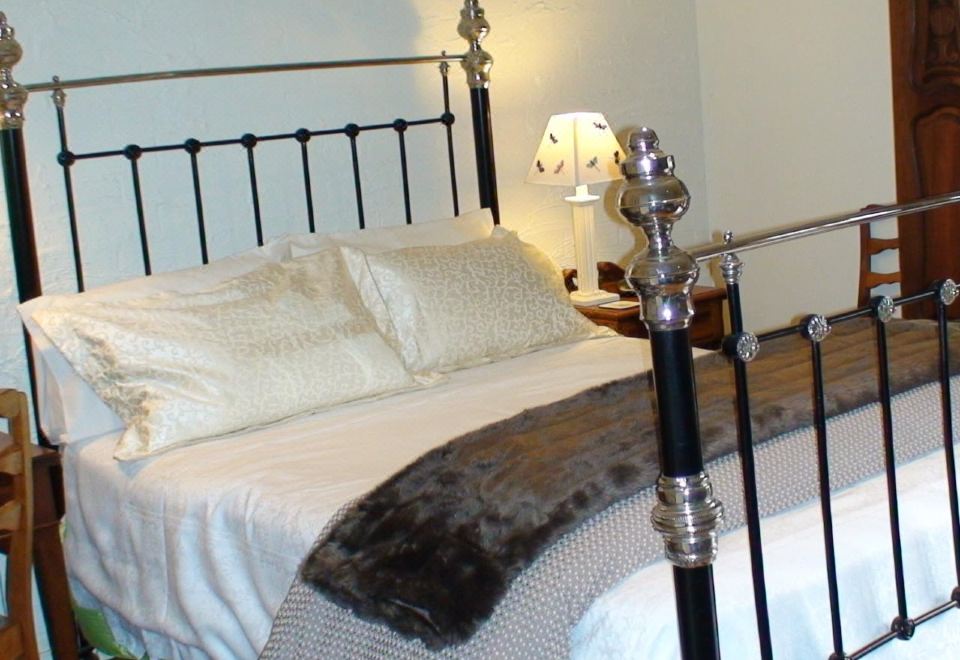 a bed with a black metal frame and white bedding is shown next to a nightstand with a lamp at Albury Cottages