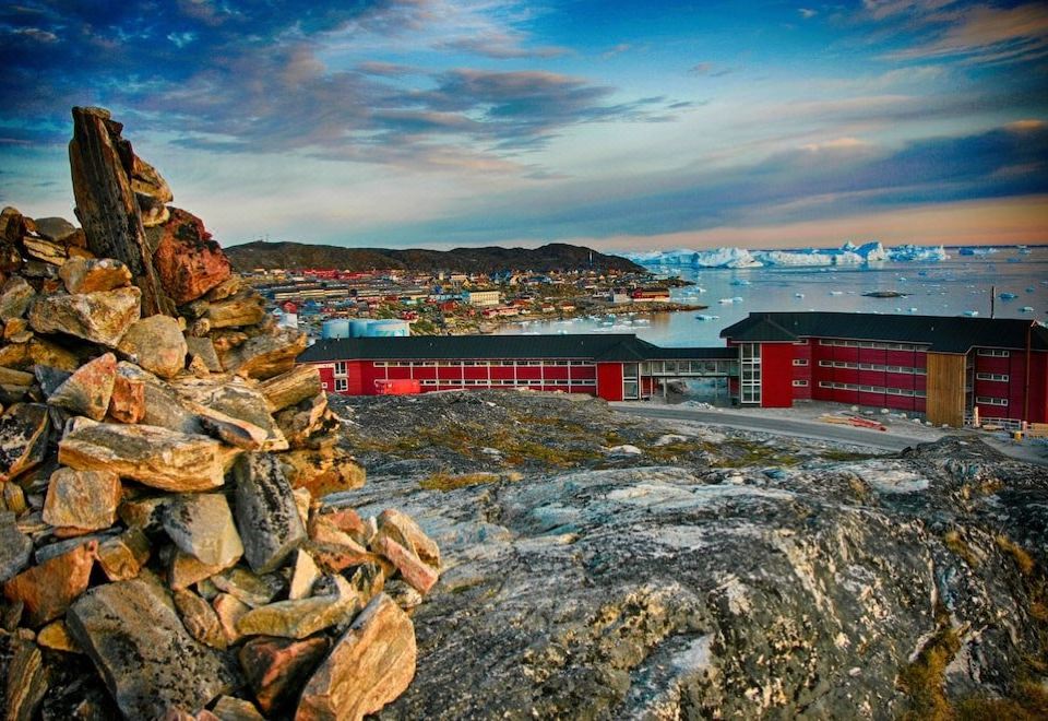 a mountain with a pile of rocks on top and buildings in the background , possibly in greenland at Hotel Arctic