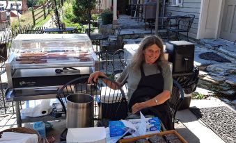 a woman standing in a backyard , preparing food on a grill and selling various items on the table at Town's Inn