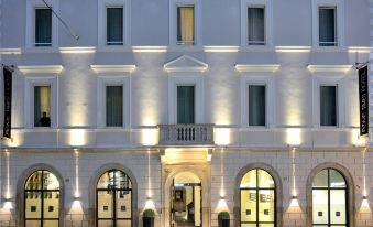 a white building with multiple entrances and windows , illuminated by lights at night , along with potted plants and a large sign at Rome Times Hotel