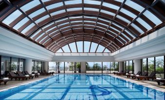 There is an indoor pool in a spacious building with a glass ceiling and windows that provide a view of the water below at Pan Pacific Hanoi