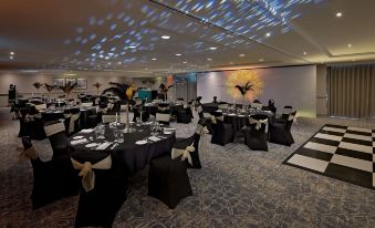 a large banquet hall with numerous dining tables and chairs , some of which are covered in black tablecloths at Hilton Cobham