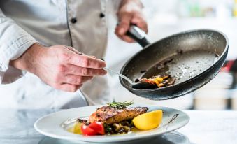 a chef in a white uniform is frying food on a pan , preparing to serve the dish at Best Western Priory Hotel