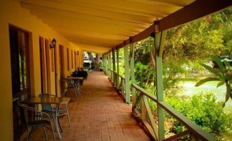 a long covered walkway with a wooden railing and tables and chairs on the right side at Ravenswood Hotel