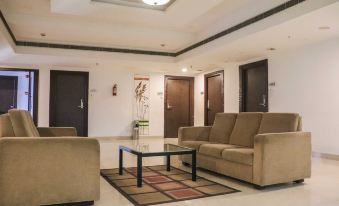 a modern living room with beige furniture , a glass coffee table , and brown carpeting , as well as two doors on the left side at Hotel Midcity