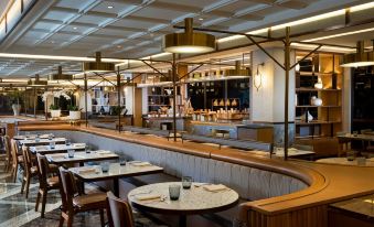 a modern restaurant with wooden tables and chairs , a bar area , and large windows with shelves at Royal Ambarrukmo Yogyakarta