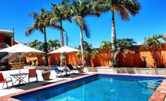 a large outdoor swimming pool surrounded by palm trees , with lounge chairs and umbrellas placed around the pool at Cactus Inn Los Cabos