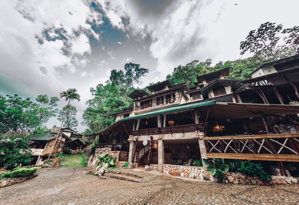 a large , two - story building surrounded by trees and mountains , with a parking lot in front of it at Altos de Cano Hondo