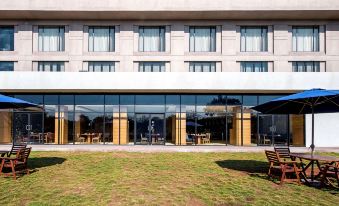 a modern building with large glass windows and wooden benches outside , giving the impression of an outdoor dining area at Hyatt Place Hampi