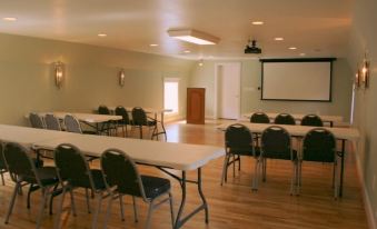 a large conference room with multiple tables and chairs , a projector screen , and wooden floors at Mountain Cove Farms Resort