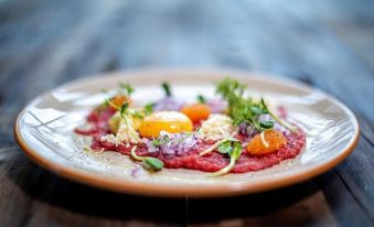 a white plate with a small amount of meat , a tomato , and a few green herbs on top at Mountain Lodge