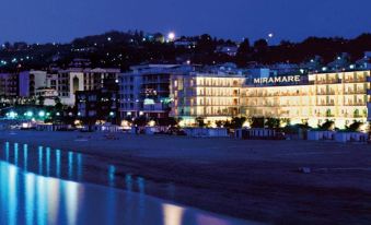 "a beachfront hotel at night , lit up and surrounded by trees and water , with the words "" hotel marmar "" displayed on the buildings" at Hotel Miramare