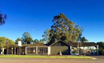 a large building with a gray roof and green trim , surrounded by trees and clear blue sky at Manjimup Kingsley Motel