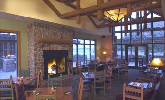a cozy restaurant with wooden tables and chairs , a fireplace , and large windows offering views of the outdoors at Quartz Mountain Resort