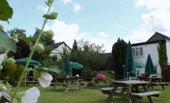 a garden with multiple picnic tables and umbrellas , surrounded by lush greenery and a house in the background at The Barford Inn