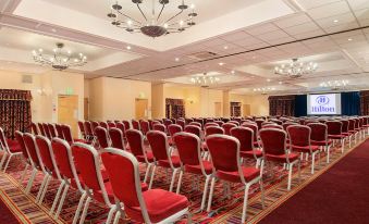 a large , empty conference room with rows of red chairs and chandeliers hanging from the ceiling at Delta Hotels Milton Keynes