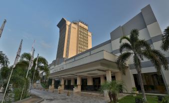 a large , modern hotel building with a long covered walkway and palm trees in front at Aryaduta Palembang