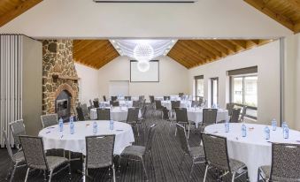 a large conference room with multiple round tables and chairs , a projector screen , and a fireplace at Mercure Goulburn