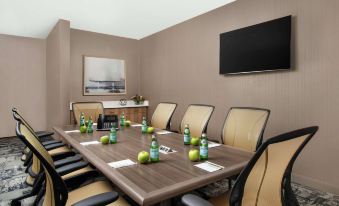 a conference room with a long table , chairs , and several apples placed on it , as well as a television mounted on the wall at Home2 Suites by Hilton Long Island Brookhaven