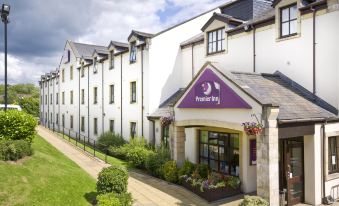 "a white building with a purple sign that says "" premier inn "" is surrounded by greenery" at Premier Inn Glasgow (Milngavie)