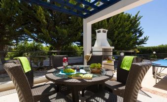 a patio area with a dining table , chairs , and a grill under a blue pergola at Panareti Coral Bay Resort