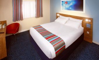 a large bed with a colorful striped blanket is in a room with blue carpet and a window at Travelodge Ludlow Woofferton
