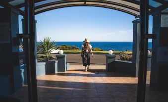 a woman in a hat is walking down a walkway with potted plants and an ocean view at Kangaroo Island Seafront