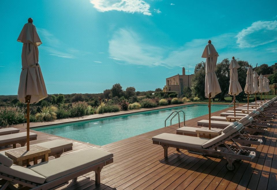 a large outdoor pool surrounded by wooden decking , with several lounge chairs placed around it at Masseria le Fabriche